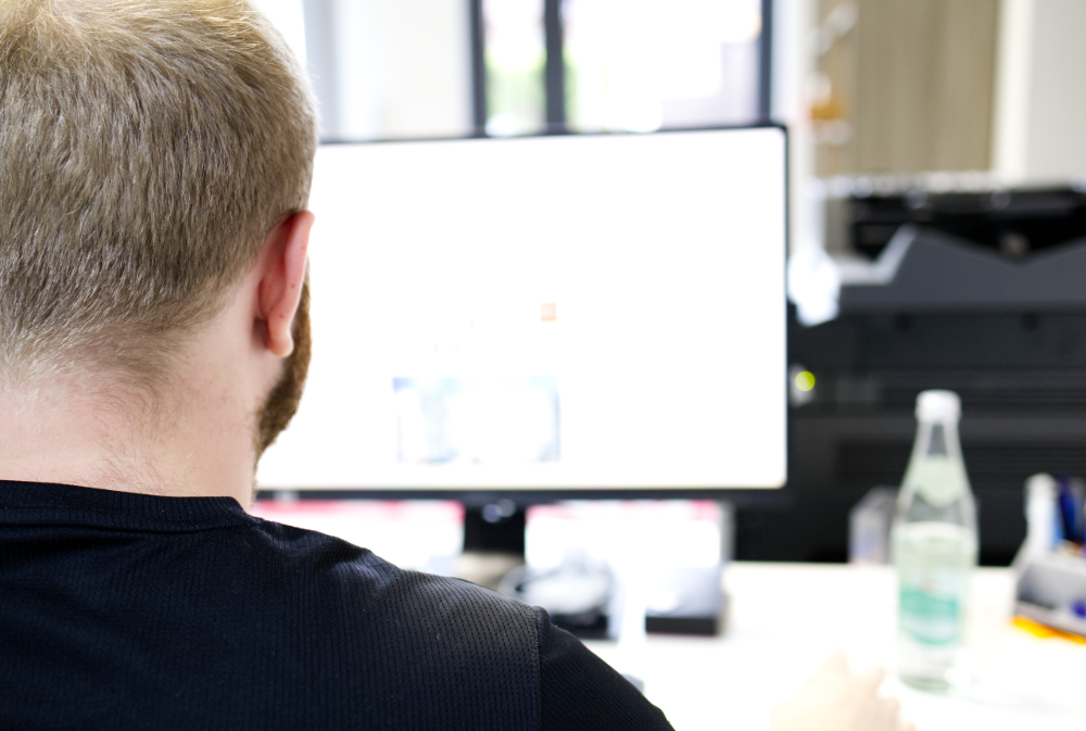 Mitarbeiter am hellen Büroarbeitsplatz vor dem Monitor — E-Mail-Sicherheit im Mittelstand: Wachsamkeit beginnt am Bildschirm